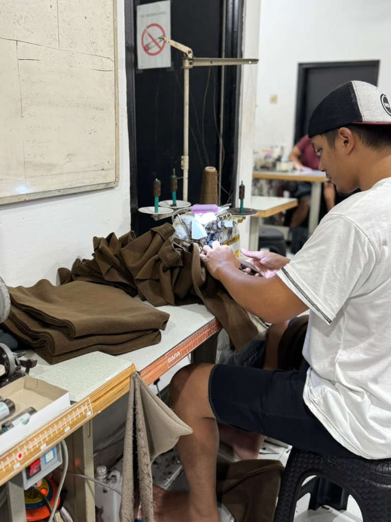 Operator Vertex mengerjakan jahitan garment di mesin overlock workshop
